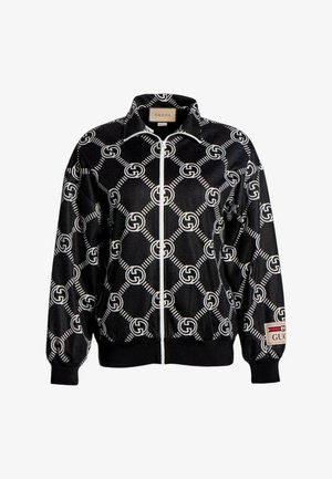 Schwarze Jacke mit Reißverschluss, weißem verschlungenem GG-Logo-Muster und Gucci-Label am Kragen und am linken Ärmelbündchen.
