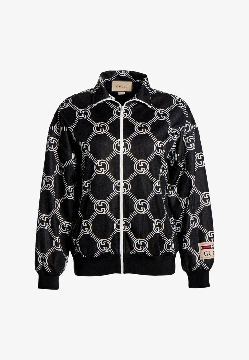 Veste noire zippée avec motif blanc du logo GG entrelacé et étiquette Gucci sur le col et le poignet de la manche gauche.