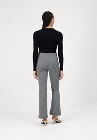 Zwarte geribbelde crop top gecombineerd met hooglopende geplooide broek in zwart en wit. Model draagt open schoenen met hakken.