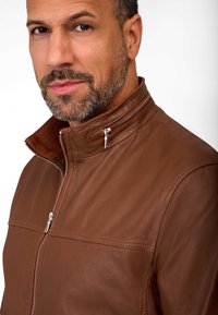Bruine leren jas met een hoge kraag, ritssluiting en een gestructureerde afwerking. Heeft contrasterende stiksels en een klein ritszakje.