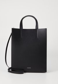Geantă tote din piele neagră, cu două mânere superioare și o curea de umăr detașabilă. Prezintă un design minimal și un logo mic în partea de jos.