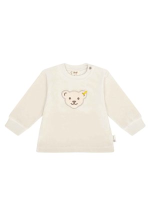 Cream long-sleeve shirt made of soft fabric featuring an embroidered bear face with a yellow accent, and snap button closure at the shoulder.