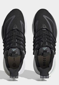 Chaussures de sport noires avec tige en mesh, lacets élastiques et semelle blanche. Présente des accents réfléchissants et des détails en textile à motifs.