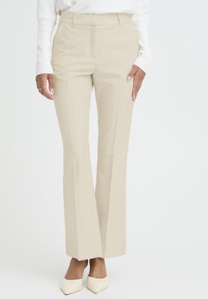 Pantaloni beige dritti su misura indossati con tacchi crema a punta e una maglia bianca a maniche lunghe, mostrati dalla vita ai piedi.