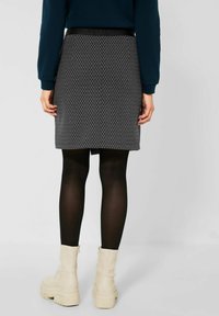 Zwart-wit gestreepte rok van jersey stof, aansluitende pasvorm, lengte tot halverwege het bovenbeen, gecombineerd met zwarte panty’s en chunky witte enkellaarsjes.