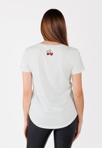 T-shirt blanc à manches courtes avec un col rond et un motif cerise imprimé dans le haut du dos. Texture lisse, coupe régulière et ourlet incurvé.
