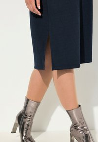 Námořnická texturovaná sukně s bočním rozparkem, doplněná metalickými stříbrnými kotníkovými botami se zipovým zapínáním a jehlovým podpatkem.