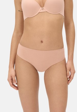 Mujer con sujetador sin costuras de color rosa claro y ropa interior tipo bikini sin costuras a juego, posando frente a un fondo neutro.