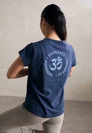 Tamno plava pamučna majica s okruglim simbolom "Om" i riječi "namaste" otisnutim svijetloplavom bojom na leđima. Uske rukave.