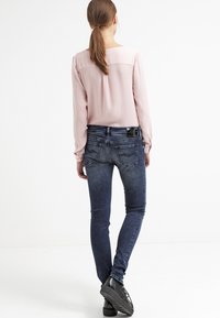 Blusa de manga larga rosa claro con escote redondeado, combinada con pantalones vaqueros skinny azul oscuro. Los pantalones presentan un diseño de bolsillo trasero y un ligero desgastado.