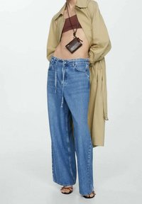 Jeans a gamba larga blu con una finitura in denim chiaro, abbinati a una camicia beige, un top corto marrone e una borsa a tracolla nera.