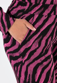 Rosa och svarta randiga leggings med en mjuk textur och sidofickdetalj. Mönstret liknar ett zebramönster i djärva färger.