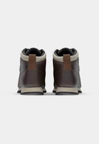 Botas de senderismo de cuero marrón con un collar gris, que presentan una suela resistente y un acento marrón en el talón. La vista trasera muestra texturas contrastantes.