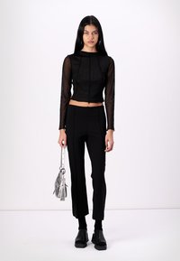 Črn crop top z prosojnimi dolgimi rokavi, v kombinaciji s črnimi oprijetimi hlačami in debelimi črnimi čevlji. Srebrna torba z nastavljivo naramnico.