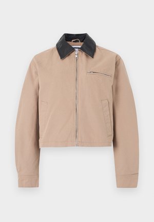 Beige jas met ritssluiting, zwarte kraag, twee zijzakken en een borstzak met rits met een subtiel geborduurd logo.