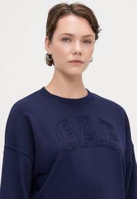 Sudadera azul marino con el logotipo bordado de "GAP". Fabricada con tejido suave, cuenta con un cuello redondo y un corte relajado.