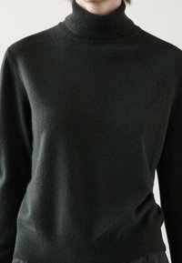 Pull col roulé vert foncé en tissu doux et texturé, avec une coupe ajustée, des poignets et un ourlet côtelés.