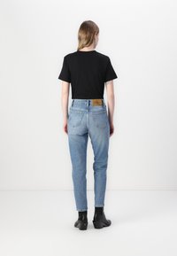 T-shirt en coton noir avec des manches courtes, associé à un jean taille haute bleu clair avec une écusson en cuir et des chaussures noires montantes.