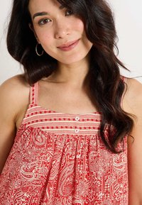 Haut à motif paisley rouge avec un design plissé, doté de fines bretelles ajustables et de boutons centrés le long du décolleté.