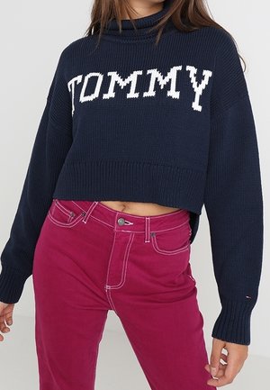Námořnický pletený zkrácený svetr s bílým nápisem "TOMMY"; spárovaný s růžovými kordovými kalhotami s vysokým pasem a kontrastním stehem.