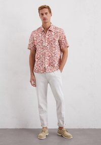 Korte mouwen overhemd met een bloemenpatroon in rood op een beige achtergrond, gecombineerd met lichte broeken en beige schoenen.