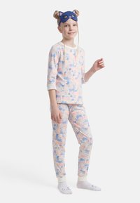 Jeune fille portant un pyjama pastel à motifs de cerfs et de fleurs, un masque bleu en forme de chat et des chaussettes blanches avec de petits visages d'animaux.