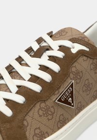 Baskets marron avec une tige en textile ornée d'un motif floral, des accents en daim, des lacets blancs et un logo triangulaire argenté.