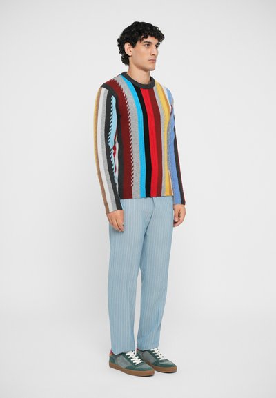 Multicolored striped sweater with a round neckline, paired with light blue striped trousers and green sneakers with brown soles.