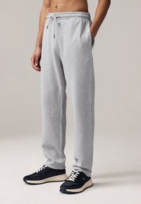 Gray sweatpants with an elastic waistband and drawstring, featuring side pockets and a relaxed fit. Paired with black athletic shoes.