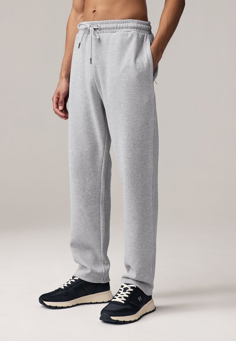 Gray sweatpants with an elastic waistband and drawstring, featuring side pockets and a relaxed fit. Paired with black athletic shoes.