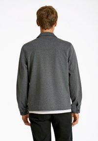 Grå långärmad jacka med en mjuk textur, knappade manschetter och krage. Baksidan har en central söm och en avslappnad passform.