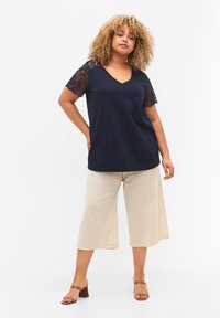 Top náutico de cuello en V con mangas cortas de encaje, combinado con pantalones de pierna ancha de color beige claro. Textura de tela suave; elegante detalle de encaje en las mangas.