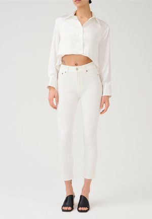 Witte cropped satijnen blouse met een puntige kraag, gecombineerd met witte high-waisted jeans. Zwarte open teen muilen maken de outfit compleet.