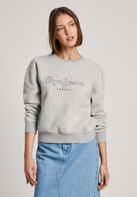 Sudadera gris con cuello y puños acanalados, que presenta el logo "Pepe Jeans London" en azul oscuro en la parte frontal. Combinada con una falda de mezclilla.
