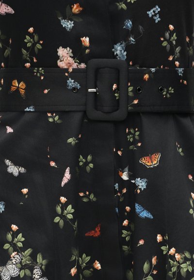 Ceinture en tissu noir avec boucle rectangulaire portée sur une robe noire ornée de papillons colorés et de petites fleurs en vert, orange, bleu et rose.