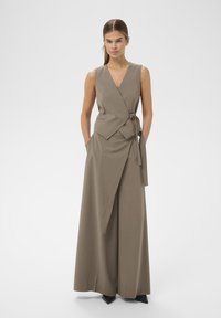 Bež brezrokavnik kombinezon z ovratnikom, pasom in širokimi hlačami. Gladek material z minimalističnim estetskim videzom.