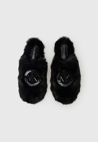 Schwarze, kuschelige Hausschuhe mit offenem Rücken und großen, runden, glänzenden MK-Logos auf der Oberseite, mit Michael Kors-Label in den Innensohlen, auf einem weißen Hintergrund.