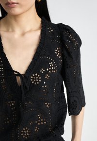 Blusa nera ricamata con ritagli floreali, scollo a V, bordi arricciati e maniche a puff lunghe fino ai gomiti, realizzata in tessuto testurizzato.