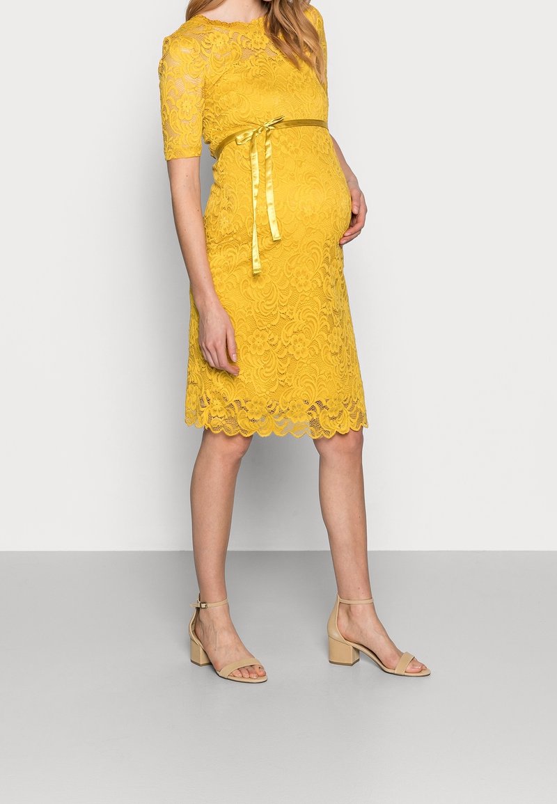 Gul spetsklänning med korta ärmar, vågig nederkant och matchande bälte. Tillsammans med beigh blockklacksandaler för att skapa en enhetlig look.