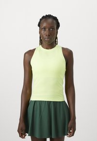 Lichtgroene mouwloze sporttop met een aansluitende pasvorm, gecombineerd met een donkergroene plissérok. Gladde structuur, minimale branding zichtbaar.