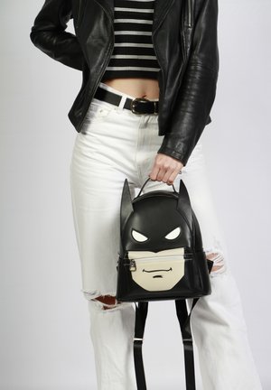Mochila negra de cuero sintético con un diseño de Batman en la parte frontal, detalles en blanco y orejas puntiagudas, con correas ajustables negras.