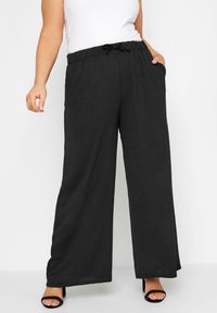 Mustat leveälahkeiset housut, jotka on valmistettu kevyestä kankaasta. Housuissa on joustava vyötärö, jossa on nyöri, sivutaskut ja väljä istuvuus.