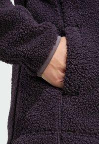 Giacca in pile viola con superficie testurizzata e soffice. Dotata di tasca laterale e polsini elasticizzati per una vestibilità aderente.