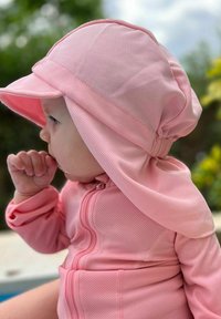 Vaaleanpunainen verkkokangas auringonpuku, jossa on huppu, vetoketjukiinnitys edessä ja pitkät hihat. Kangas on kevyt ja suunniteltu tarjoamaan suojaa auringolta.