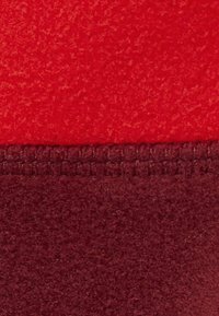 Tessuto in pile rosso e bordeaux, con una consistenza morbida; presenta una cucitura visibile tra i due colori.