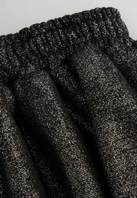 Czarny, błyszczący materiał z marszczoną gumką w pasie. Tekstura zawiera drobne metaliczne drobinki na gładkiej powierzchni.