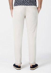 Helle beige Hose mit geradem Schnitt, aus Baumwollmaterial, zwei Gesäßtaschen und umgeschlagenen Säumen, kombiniert mit schwarzen Espadrilles.
