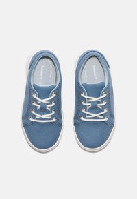 Blå canvas sneakers med vita gummisulor, som har vita snören och sömmar, samt en rundad tådesign. Botten är texturerad för bättre grepp.