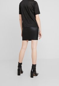 Svart kortärmad topp med vertikala glittrande ränder, kombinerad med en svart minikjol i konstläder och svarta ankelstövlar med klack.