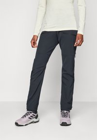 Pantalons noirs d'extérieur avec de multiples poches zippées, fabriqués à partir d'un matériau léger, associés à des chaussures de randonnée violettes. Présente un design épuré.